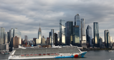 A shot of a cruise ship along the Hudson River in front of Hudson Yards and the Empire State Building in New York