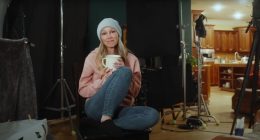 Woman holding a mug, sitting on a chair on a film set.