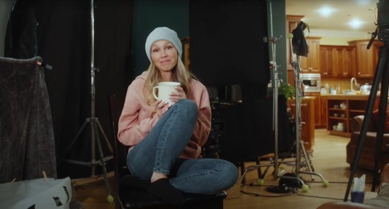 Woman holding a mug, sitting on a chair on a film set.