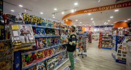 A masked employee stocking shelves in a toy store.