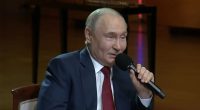 Vladimir Putin speaking into a microphone, stating that love is shown in ways beyond kissing and hugging.