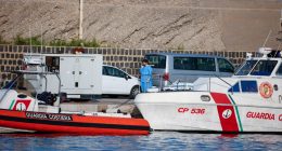 Person on phone near Guardia Costiera boat at port.