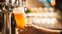 A hand holding a pint glass of beer being poured from a tap.