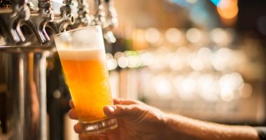 A hand holding a pint glass of beer being poured from a tap.