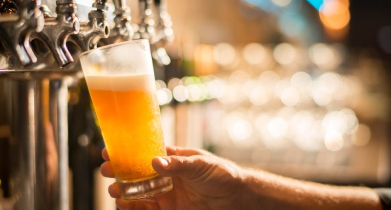 A hand holding a pint glass of beer being poured from a tap.
