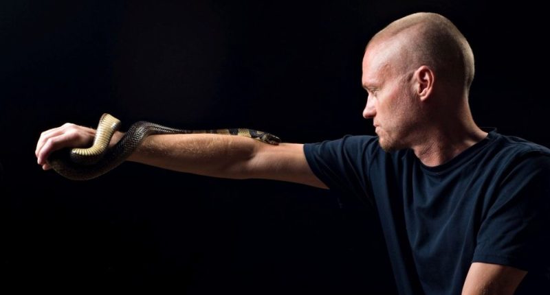 Man with hyper-immunity to snake venom holding a water cobra.