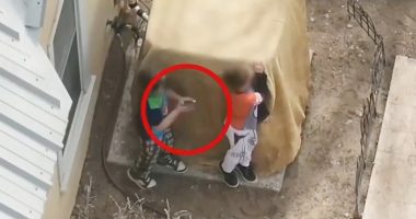 Overhead view of two boys behind a covered object, one appearing to hold a gun.