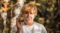 Senior woman smoking a cigarette in a forest.