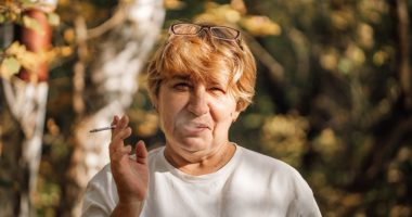 Senior woman smoking a cigarette in a forest.