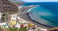 Aerial view of Tazacorte, La Palma, showing a black sand beach, colorful buildings, and a marina.