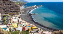 Aerial view of Tazacorte, La Palma, showing a black sand beach, colorful buildings, and a marina.