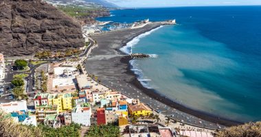 Aerial view of Tazacorte, La Palma, showing a black sand beach, colorful buildings, and a marina.