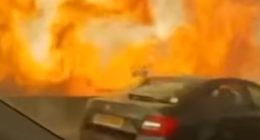 Cars driving on a highway next to a large wildfire.