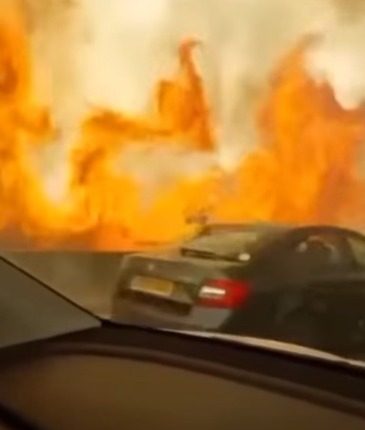 Cars driving on a highway next to a large wildfire.
