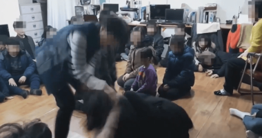 A person interacting with a group of children sitting on the floor.