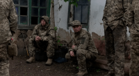 Soldiers in camouflage resting near a building.