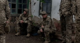Soldiers in camouflage resting near a building.