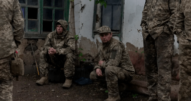 Soldiers in camouflage resting near a building.