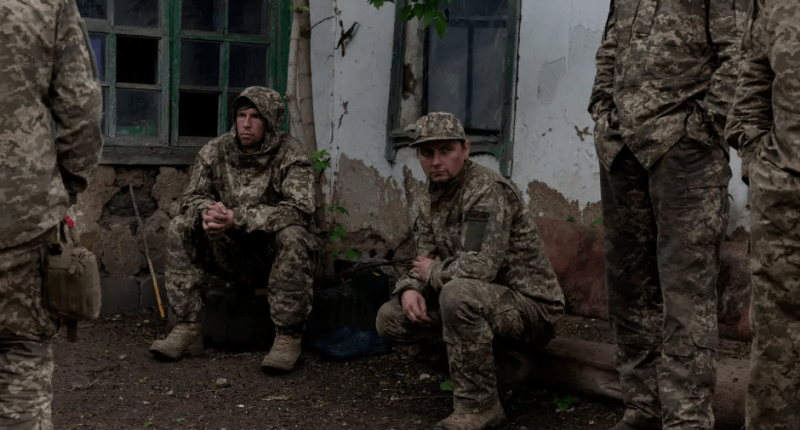 Soldiers in camouflage resting near a building.
