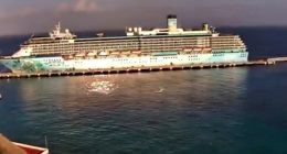Cruise ship docked at a port with a UFO-like object zooming past.