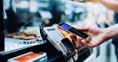 Woman using smartphone to make contactless payment at a cafe.
