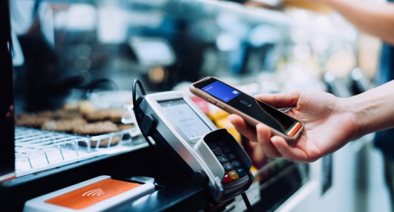 Woman using smartphone to make contactless payment at a cafe.