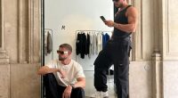 Two men in sunglasses and casual attire sitting outside a store.