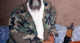 Osama bin Laden sitting with an AK-47.