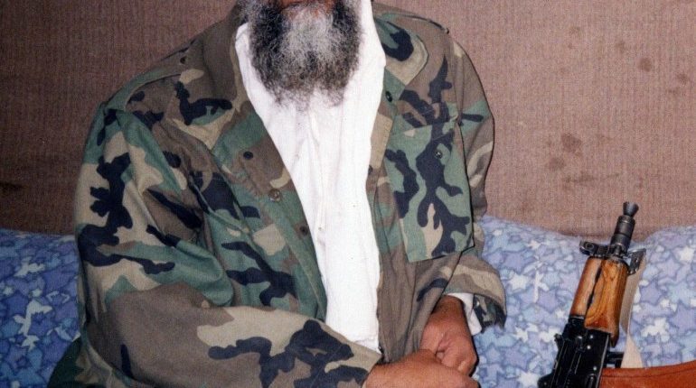 Osama bin Laden sitting with an AK-47.