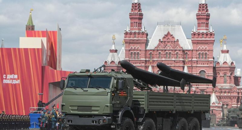 Armored vehicle carrying drones in a military parade.
