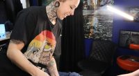 A photo of Kat Farris, a tattoo artist from Enova Ink and Body Art, showing a client a tattoo sketch to cover a self-harm tattoo.