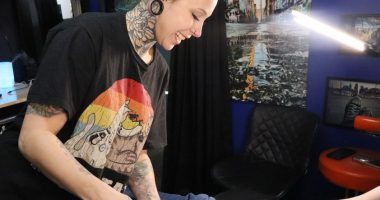 A photo of Kat Farris, a tattoo artist from Enova Ink and Body Art, showing a client a tattoo sketch to cover a self-harm tattoo.