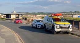 Coastguard vehicle and cars near a beach.