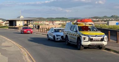 Coastguard vehicle and cars near a beach.