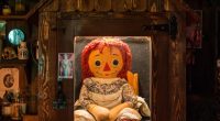 Annabelle doll behind glass with warning sign, viewed by a girl.