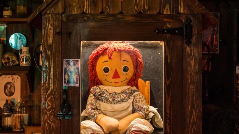 Annabelle doll behind glass with warning sign, viewed by a girl.