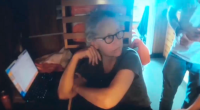 Screenshot of a woman sitting at a laptop.