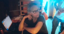 Screenshot of a woman sitting at a laptop.