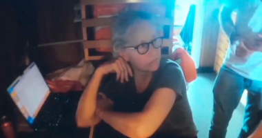 Screenshot of a woman sitting at a laptop.