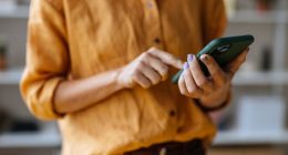 A close up view of an unrecognizable Caucasian entrepreneur texting on her smartphone while standing indoors.
