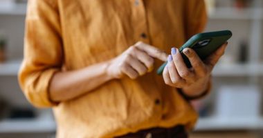 A close up view of an unrecognizable Caucasian entrepreneur texting on her smartphone while standing indoors.