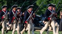 Soldiers in Revolutionary War-era uniforms charging during a US Army Twilight Tattoo event.