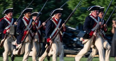 Soldiers in Revolutionary War-era uniforms charging during a US Army Twilight Tattoo event.