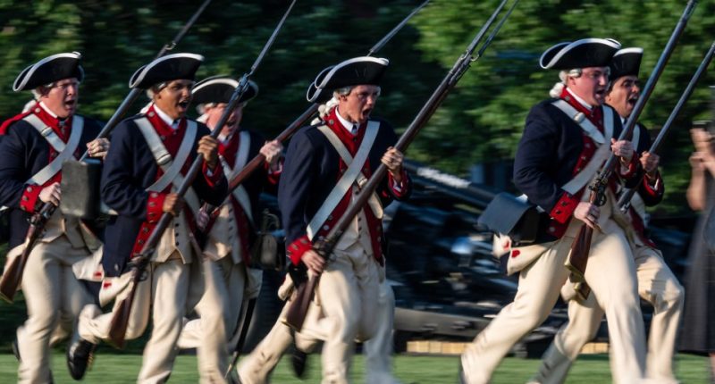Soldiers in Revolutionary War-era uniforms charging during a US Army Twilight Tattoo event.