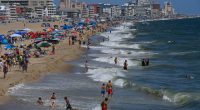 Crowded beach with people swimming and relaxing under umbrellas.