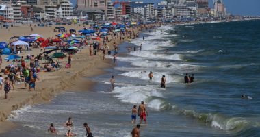 Crowded beach with people swimming and relaxing under umbrellas.