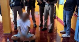 A Buddhist monk sits on the floor surrounded by police officers.