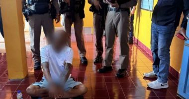 A Buddhist monk sits on the floor surrounded by police officers.