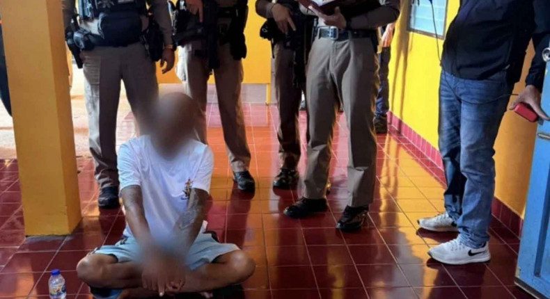 A Buddhist monk sits on the floor surrounded by police officers.