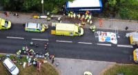 Aerial view of a double-decker bus in a river, surrounded by emergency responders and bystanders.